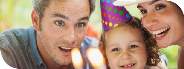 Two parents standing on either side of their toddler wearing a birthday party hat.